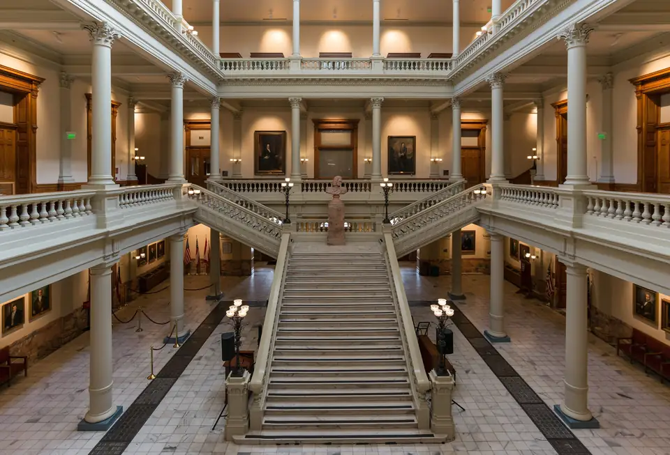 A grand staircase rising through a columned atrium with pale veined marble floors.
