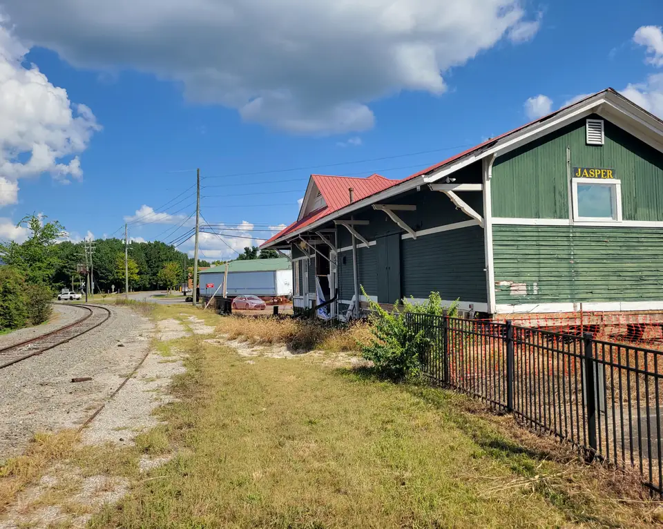 A green clapboard railroad depot with a red roof and a yellow JASPER sign beside a curving track.