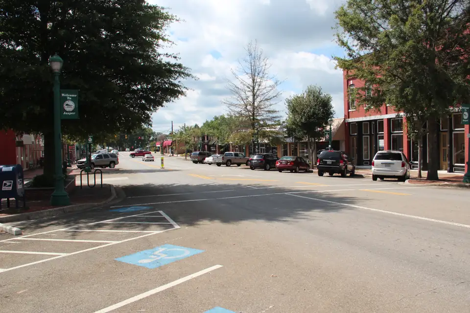 Brick storefronts and parked cars on a tree-lined downtown street, with a green Welcome to Jasper banner on a lamppost.