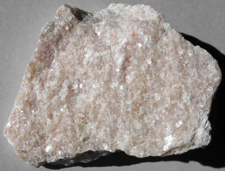 A fist-sized sparkling white marble specimen with a pink blush and a few greenish streaks.