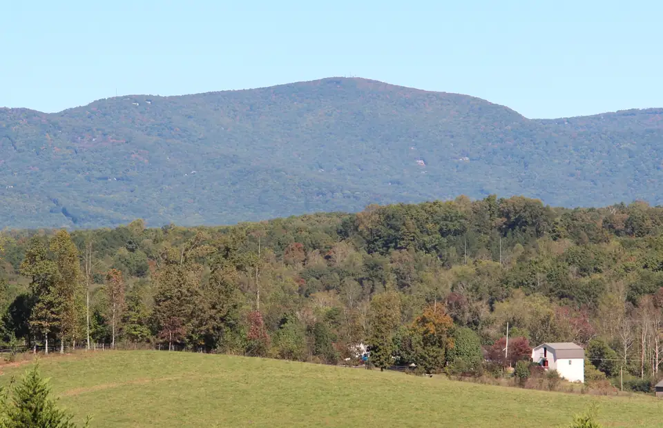 A broad forested mountain with the first fall color, above gold and red hardwoods and a green pasture.