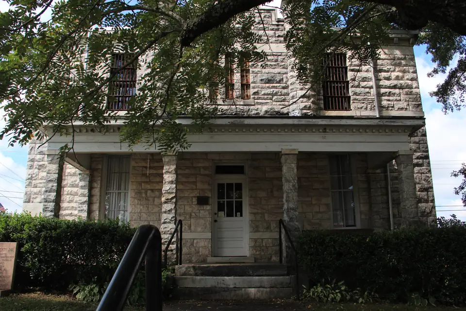 A two-story building of rough pale stone blocks with barred upper windows and a white front porch.