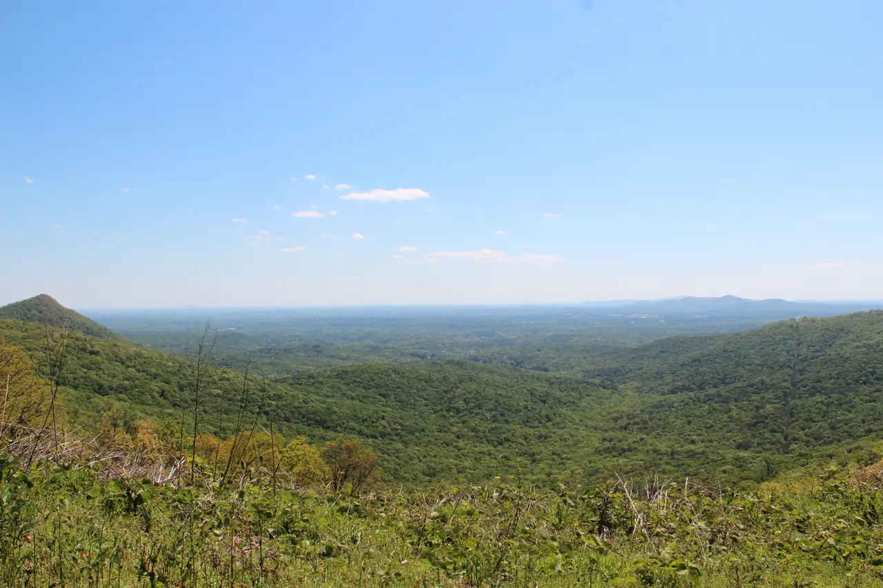 A long view from a high overlook across rolling green forested ridges fading into haze.
