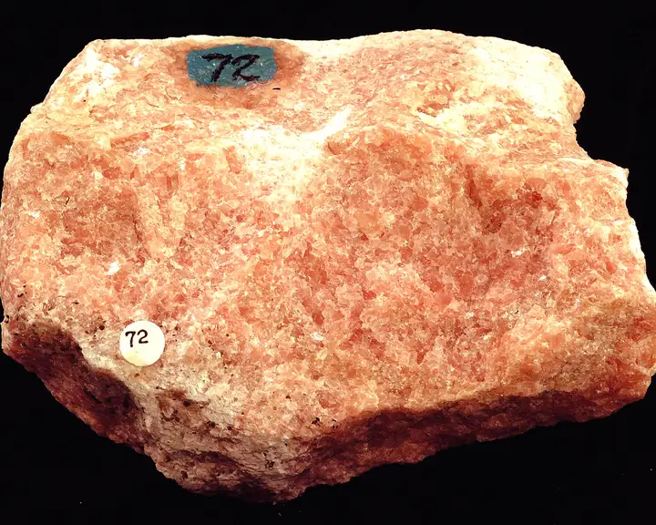 A salmon-pink, coarse-grained marble specimen with white patches on a black background.