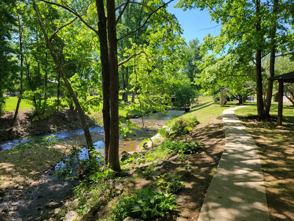 A shallow rocky creek winding through dappled shade beside a curving footpath and sunny lawns.