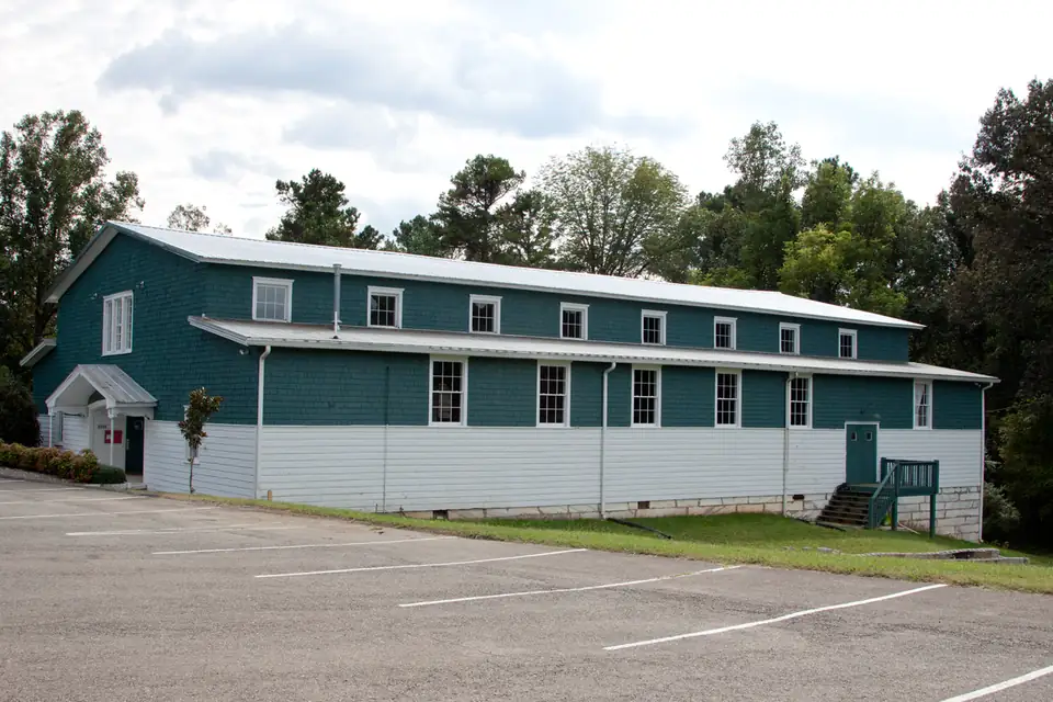 A long two-story gym with teal shingle siding above white lap siding and rows of white-trimmed windows.