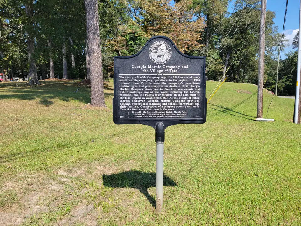 A black Georgia Historical Society marker titled Georgia Marble Company and the Village of Tate, in a grassy lot with pines.